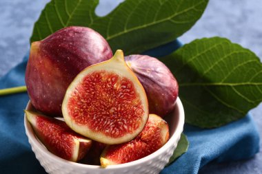 Taze incirlerle dolu bir kase ve grunge mavisi arka planda bitki yaprağı