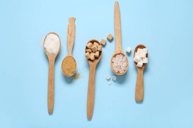 Mavi arka planda farklı tipte şeker içeren kaşıklar