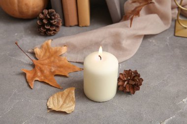 Sonbahar yapraklarıyla yanan mum ve gri arka planda çam kozalakları