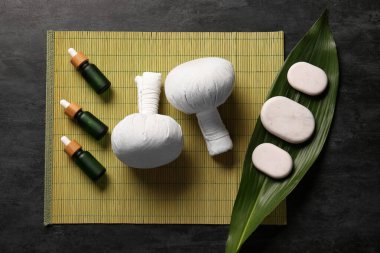 Siyah arka planda bitkisel torbalar, taşlar ve gerekli yağ şişeleriyle güzel bir spa kompozisyonu.