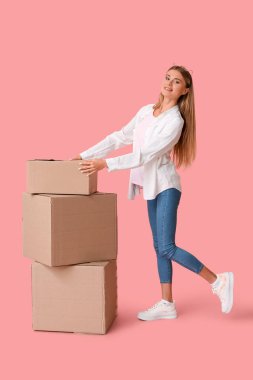 Pembe arka planda karton kutuları olan güzel bir genç kadın. Taşınma konsepti