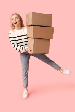 Mutlu genç bir kadın pembe arka planda karton kutular tutuyor. Yeni ev konseptine geçiyoruz.