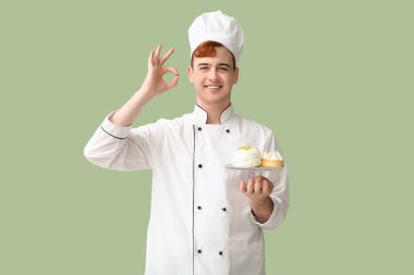 Üniformalı bir erkek pastacı elinde lezzetli tatlılar ve yeşil arka planda iyi bir jest gösteriyor.