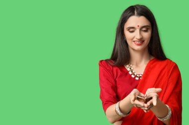 Yeşil arka planda diya lambası olan sarili güzel bir Hintli kadın. Divaly kutlaması