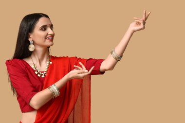 Sari giymiş, kahverengi arka planda dans eden güzel bir Hintli kadın. Divaly kutlaması