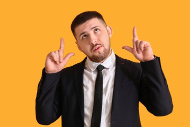 Düşünceli genç işadamı sarı arka planda bir şeye işaret ediyor. İş fikri kavramı
