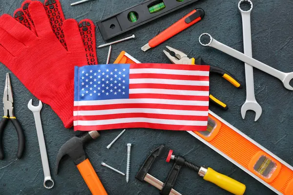ABD bayraklı kompozisyon, eldivenler ve koyu grunge arka planda farklı aletler. İşçi Bayramı kutlamaları