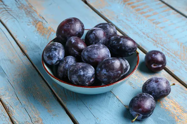 Mavi ahşap arka planda taze erikli kase
