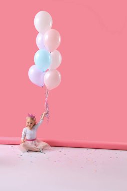 Güzel balonları olan sevimli küçük kız pembe arka planda oturuyor.