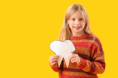 Sağlıklı dişleri ve sarı arka planda kağıt dişleri olan mutlu küçük kız.