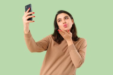 Cep telefonlu genç bir kadın yeşil arka planda görüntülü sohbet ediyor. Çevrimiçi randevu kavramı