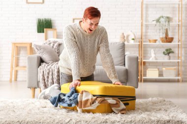 Evde bavulu kapatmaya çalışan duygusal genç adam.