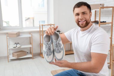 Butikte bir çift şık spor ayakkabı tutan mutlu genç adam.