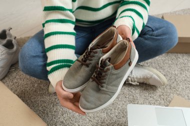 Bir adam yerde otururken şık ayakkabılar tutuyor.