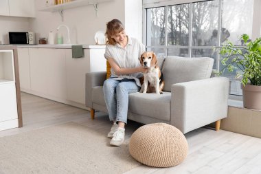 Evdeki kanepede oturan sevimli av köpekli genç kadın.