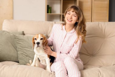 Evdeki kanepede oturan sevimli av köpekli genç kadın.