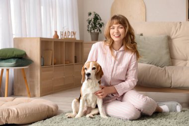 Evde halıda oturan sevimli av köpeği olan genç bir kadın.