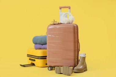 Sarı arka planda kalın elbiseli bavullar.