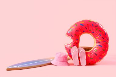 Şişirilebilir yüzüklü sörf tahtası, parmak arası terlikler ve pembe arka planda panama şapkası. Yaz tatili kompozisyonu