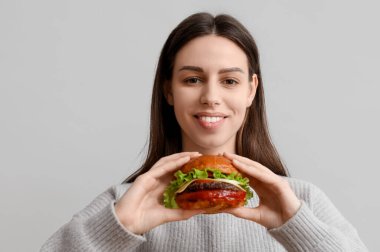 Beyaz arka planda lezzetli bir burgerle gülümseyen genç kadın.
