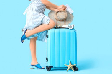 Mavi arka planda bavulu ve plaj aksesuarları olan bir bayan gezgin.