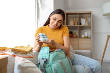 Hamile bir kadın doğum çantasına bebek paçası yerleştiriyor.