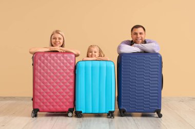 Bej duvarın yanında bavullu mutlu bir aile.