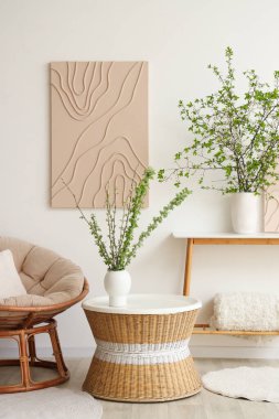 Rahat koltuk, kahve masası ve aydınlık oturma odasında çiçek açan dalları olan vazolar.