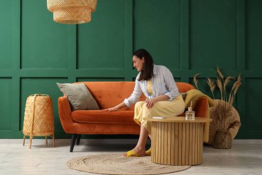 Evdeki yeşil duvarın yanındaki kırmızı koltukta oturan genç kadın.