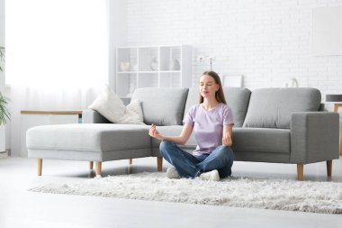 Genç ve güzel bir kadın şık bir oturma odasında yerde meditasyon yapıyor.