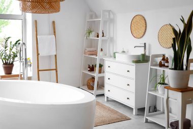 Banyonun içinde beyaz küvet, çekmeceler ve ev bitkileri var.