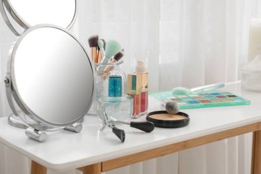 Dekoratif kozmetik setiyle giyinme masası, aynalar ve parfüm şişesi.