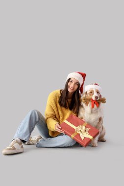 Avustralyalı çoban köpeği olan genç bir kadın. Noel Baba şapkası takıyor ve arka planda Noel hediyeleri var.