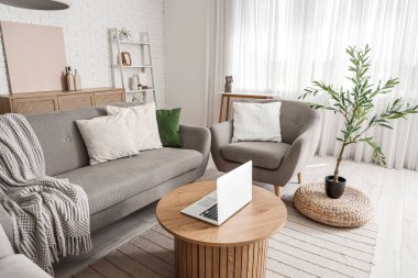 Rahat kanepesi, koltuğu, kahve masası, dizüstü bilgisayarı ve zeytin ağacı olan şık bir oturma odası.