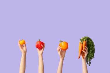 Female hands holding fresh vegetables on lilac background