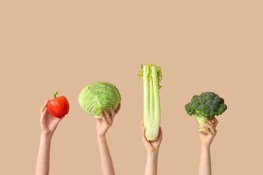 Female hands holding fresh vegetables on beige background