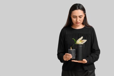 Morg vazosu, yanan mum ve beyaz arka planda zambak çiçeği olan genç bir kadın.