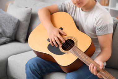 Genç çocuk evde gitar çalıyor, yakın plan.