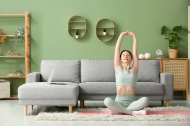 Güzel genç bir kadın oturma odasında yoga yapıyor.