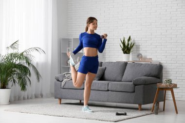 Oturma odasında dambılla antrenman yapan güzel bir genç kadın.