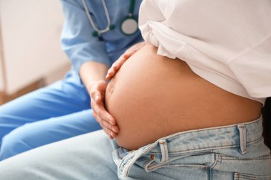 Kadın doktor klinikte genç hamile kadını muayene ediyor.