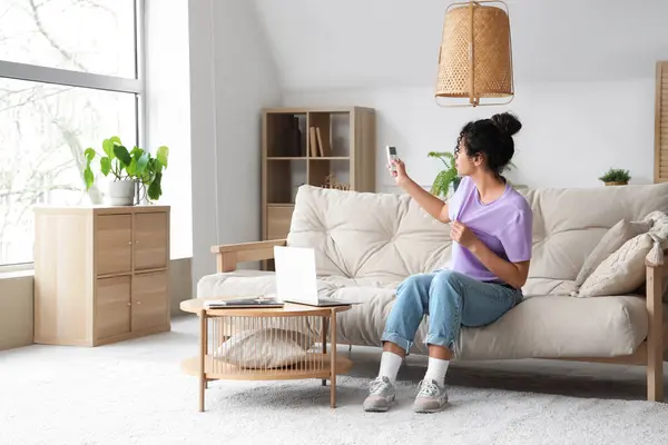 stock image Young African-American woman turning on air conditioner at home