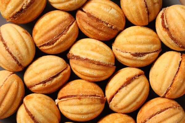 Tasty walnut shaped cookies with boiled condensed milk as background, closeup