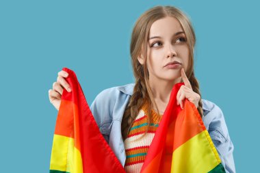 Mavi arka planda LGBT bayrağı olan düşünceli genç kadın, yakın plan.