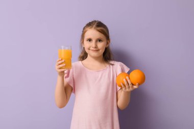 Bir bardak meyve suyu ve arkaplanda portakallar olan tatlı küçük bir kız.