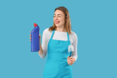 Deterjan şişesi ve mavi arka planda tuvalet fırçası olan genç bir kadın.