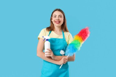 Mavi arka planda deterjan ve toz bezi olan genç bir kadın.