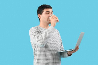 Dizüstü bilgisayarı olan erkek programcı mavi arka planda kahve içiyor.