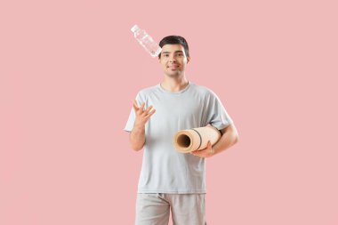 Pembe arka planda bir şişe su ve spor paspası olan genç bir adam.