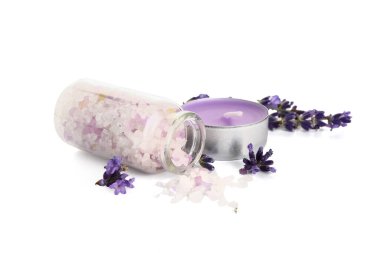 Beyaz arka planda bir şişe deniz tuzu, mum ve lavanta çiçeği.